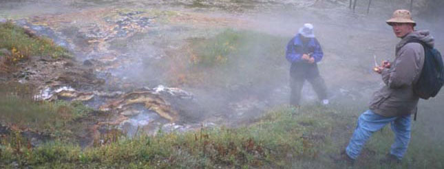 Two researchers surveying a thermal area with mat community.