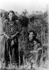 Crow women in traditional Elk tooth dresses, one sitting and holding a baby.
